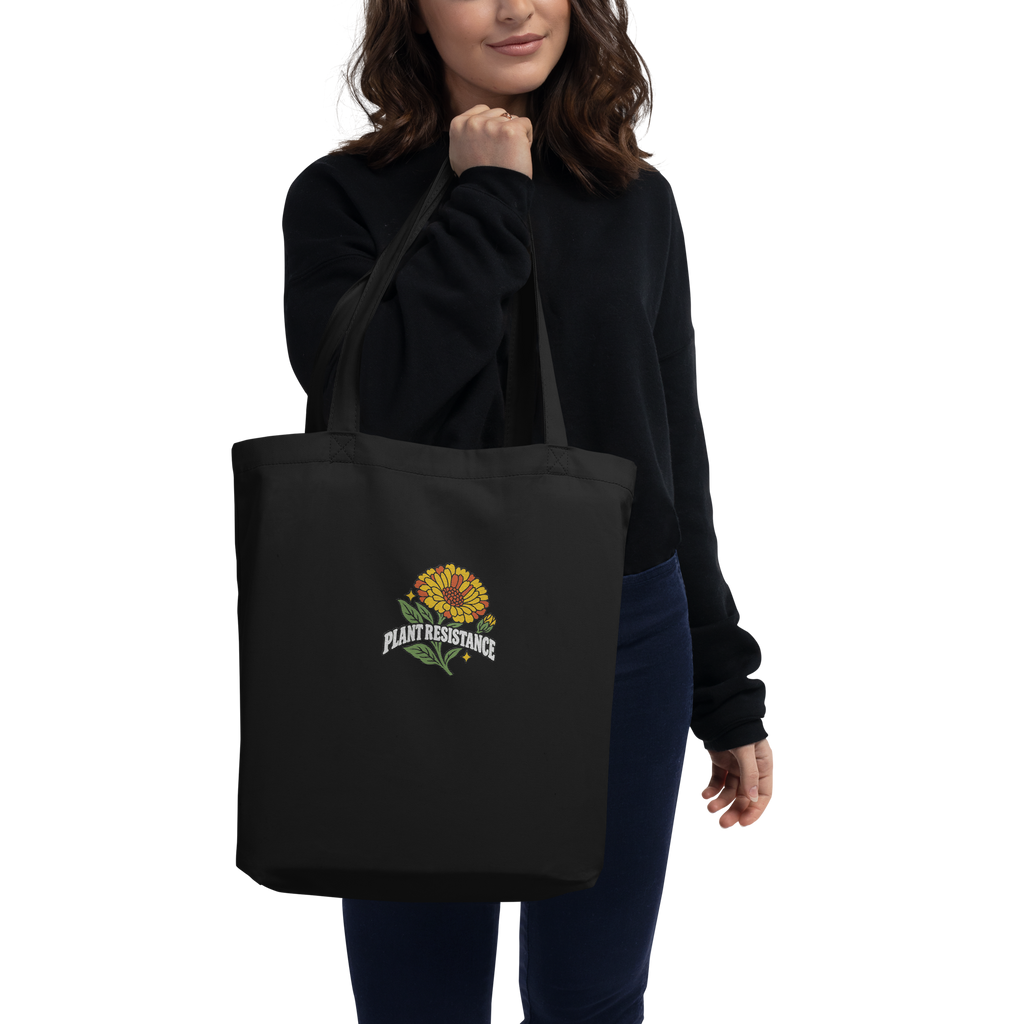 Black organic cotton tote bag with embroidered Plant Resistance calendula design. Schwarze Bio-Baumwolltasche mit gesticktem Plant Resistance Ringelblumen-Design.