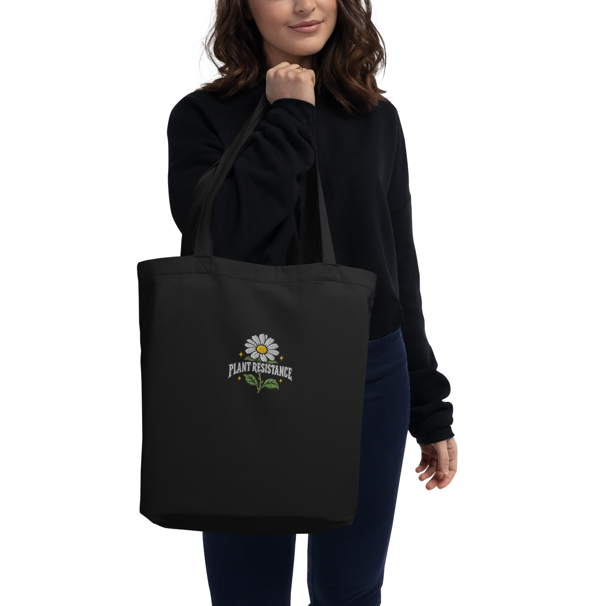 Black organic cotton tote bag with embroidered Plant Resistance daisy design. Schwarze Bio-Baumwolltasche mit gesticktem Plant Resistance Gänseblümchen-Design.