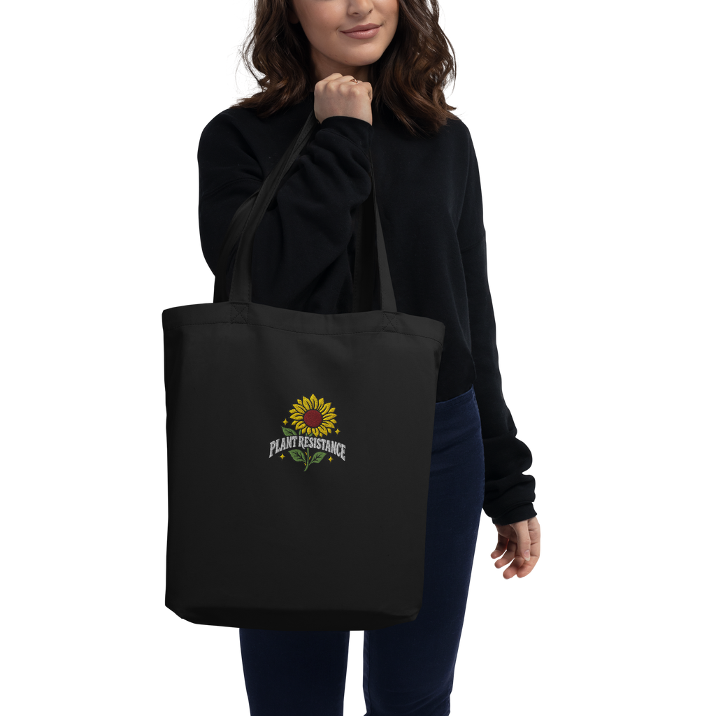Black organic cotton tote bag with embroidered Plant Resistance sunflower design. Schwarze Bio-Baumwolltasche mit gesticktem Plant Resistance Sonnenblumen-Design.